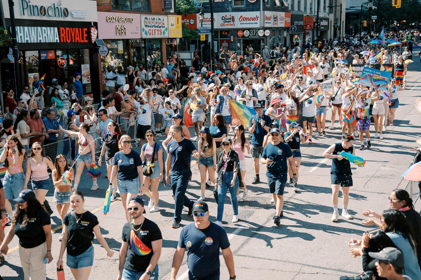 Participants march in a vibrant street parade, celebrating with rainbow flags and colorful attire, as onlookers cheer from the sidelines.