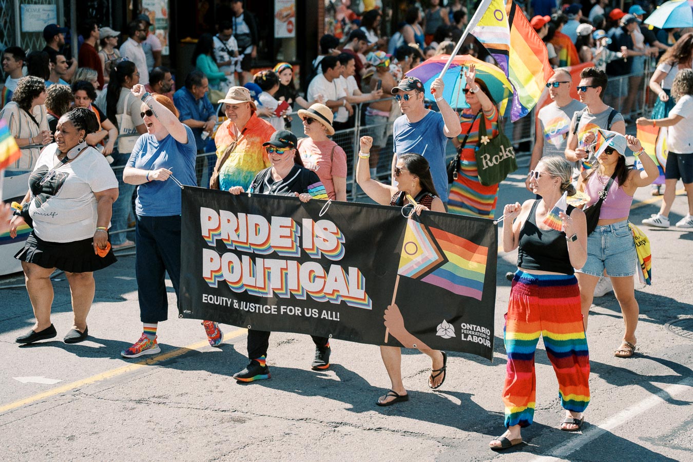 Participants in a Pride parade march with a banner reading 'Pride is Political', advocating for equity and justice.