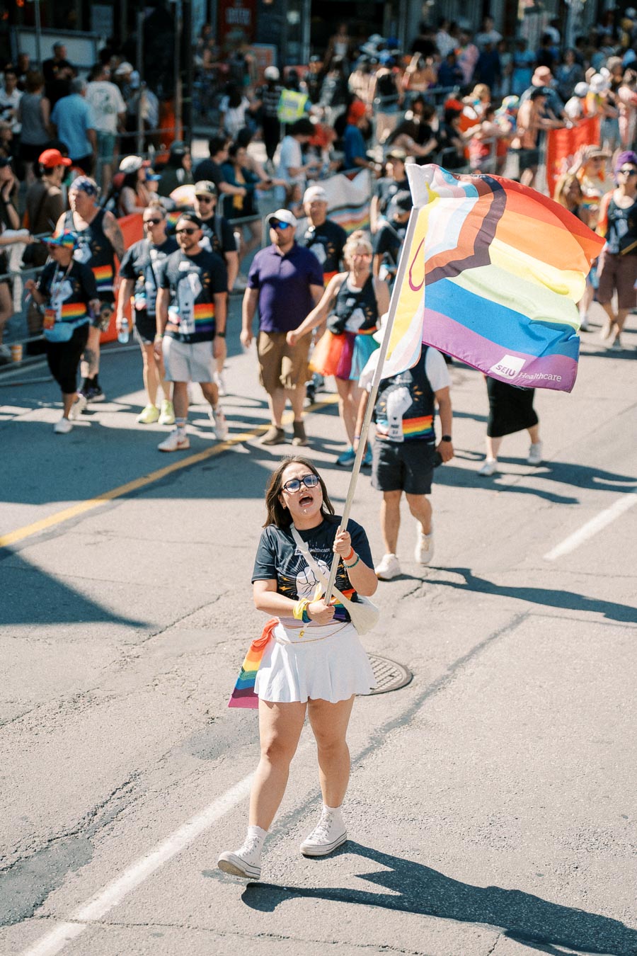 A participant proudly waves a rainbow flag during a lively pride parade, surrounded by a diverse crowd celebrating inclusivity and diversity.