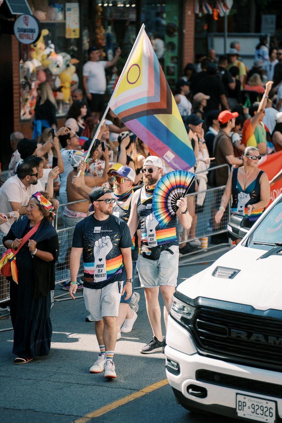 Participants in a pride parade march with a rainbow flag and wear shirts with pride-themed designs, celebrating diversity and inclusion.