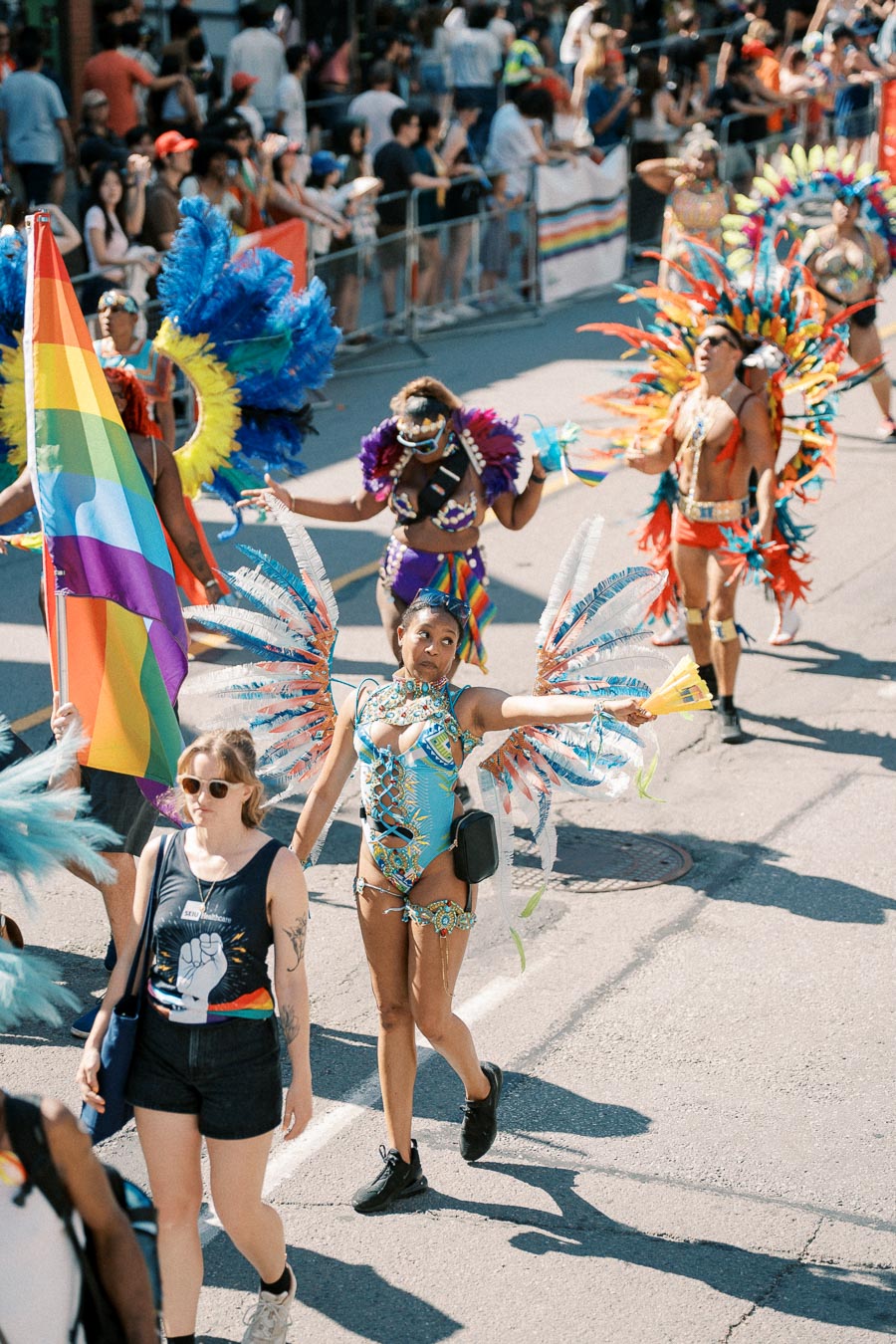 Participants in colorful costumes and a rainbow flag at a lively parade.
