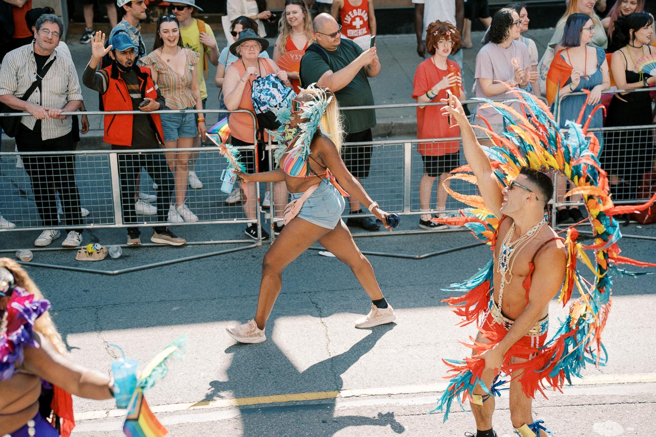 Participants in vibrant, feathered costumes parade down the street, entertaining a crowd of onlookers during a lively festival.