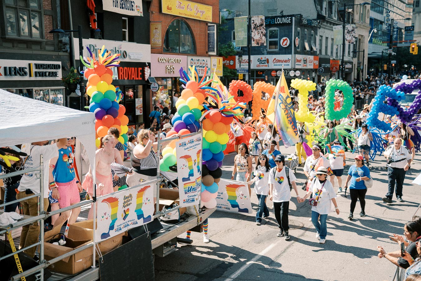 A lively scene from a Pride parade featuring participants with rainbow balloons and colorful attire, celebrating diversity and inclusion.