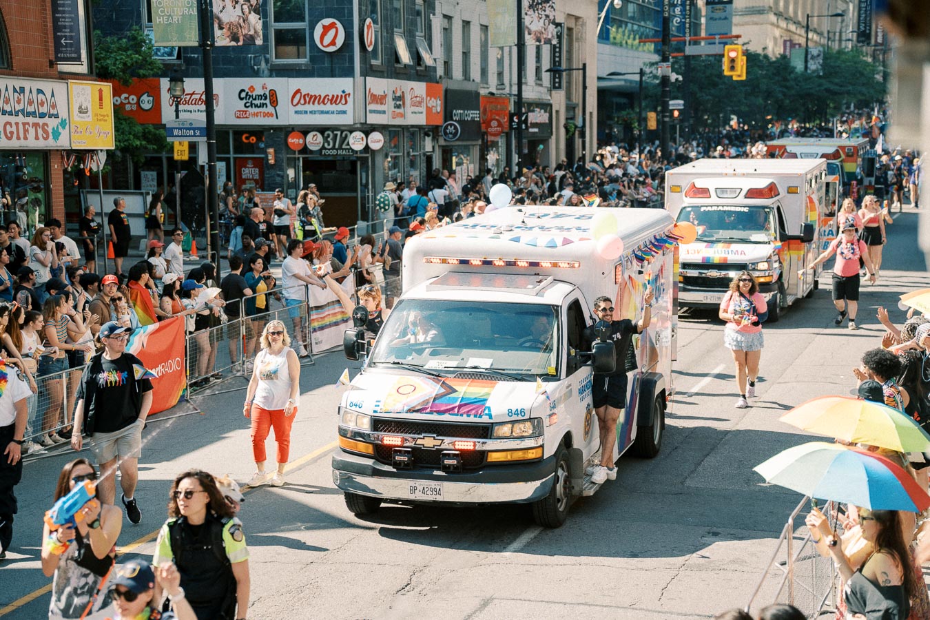A vibrant parade featuring decorated ambulances and participants celebrating on a city street, with spectators lining the sidewalks.