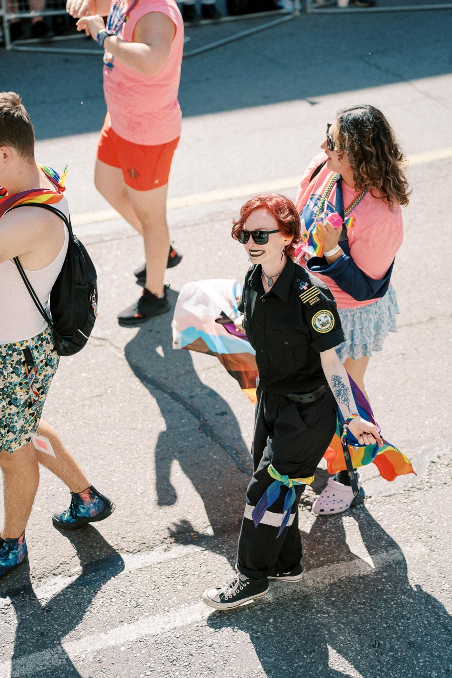 Participants in a pride parade walk down the street, adorned in colorful attire and carrying pride flags, celebrating diversity and inclusion.