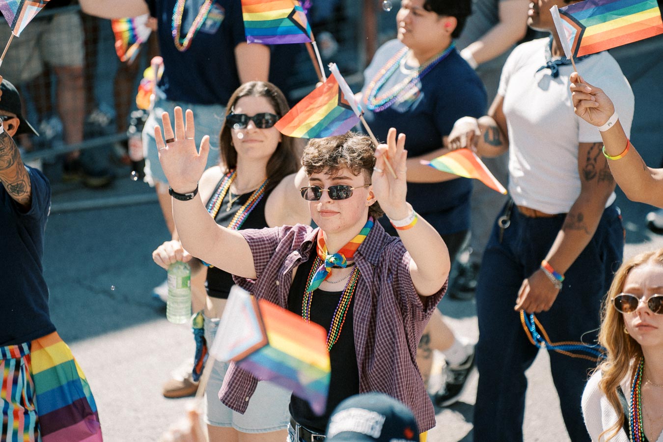 Participants in a pride parade wave rainbow flags and wear colorful accessories, celebrating diversity and inclusion.