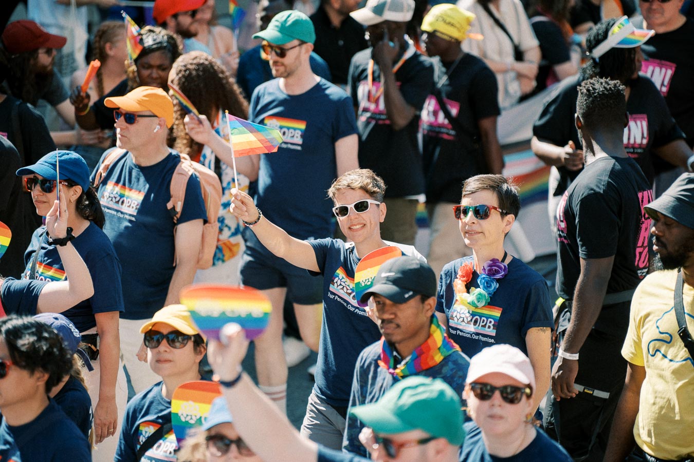 Participants at a pride parade celebrate with rainbow flags and colorful attire, showcasing support for the LGBTQ+ community.