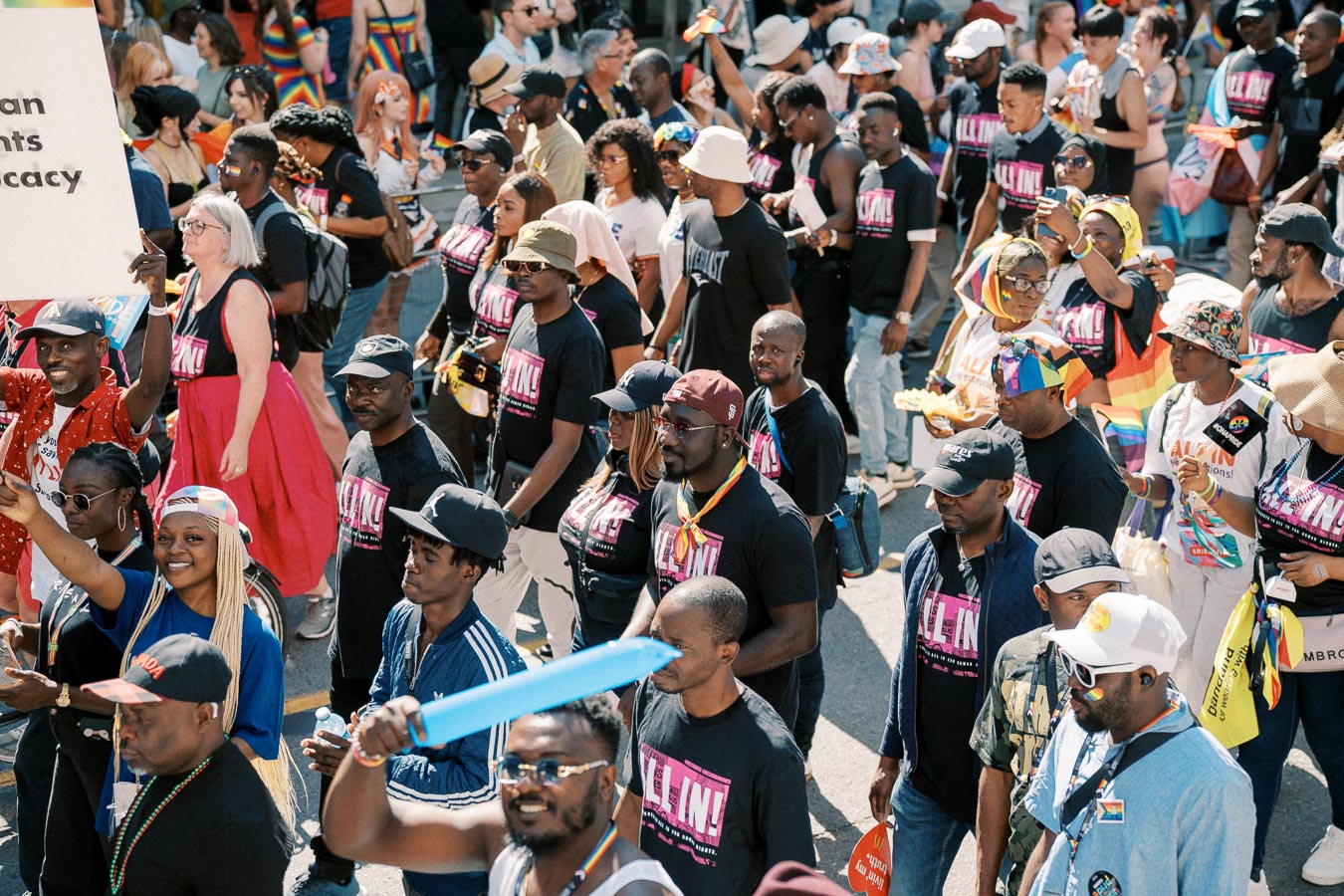 A vibrant pride parade with participants wearing "ALL IN!" T-shirts, celebrating diversity and inclusion.