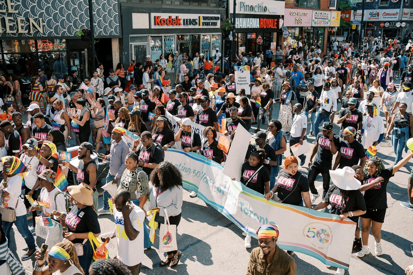 Participants in a vibrant pride parade march down a busy street, celebrating diversity and inclusion with banners and rainbow-themed accessories.