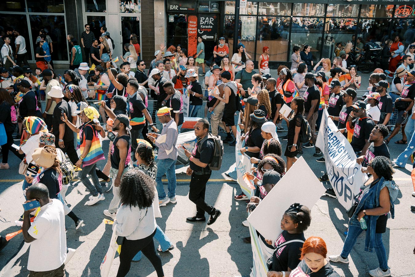 Participants in a pride parade march down a city street, showcasing diversity and unity with colorful attire and banners.