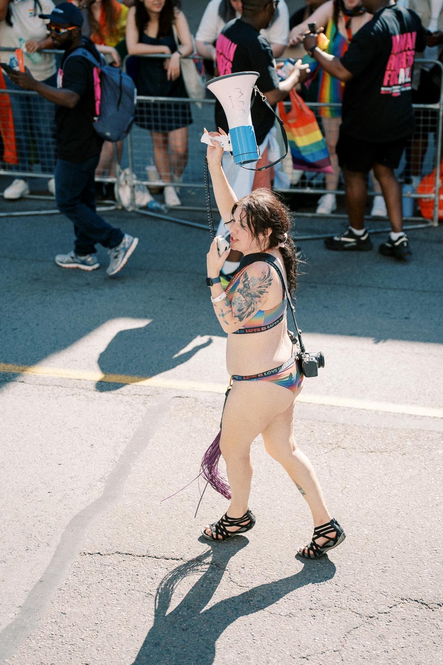 A participant in a rainbow bikini with a megaphone at a pride parade.