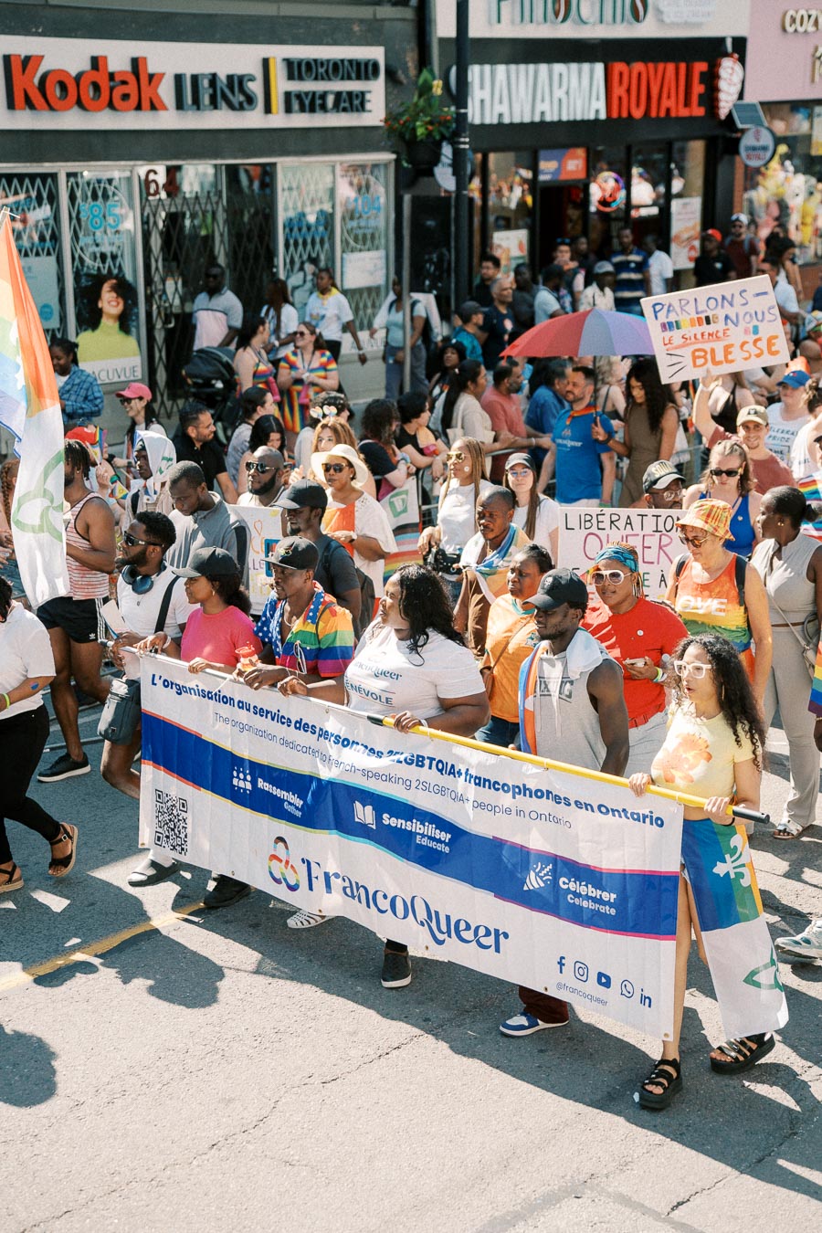 Participants in a parade march with a banner for FrancoQueer, supporting French-speaking LGBTQIA+ individuals in Ontario.