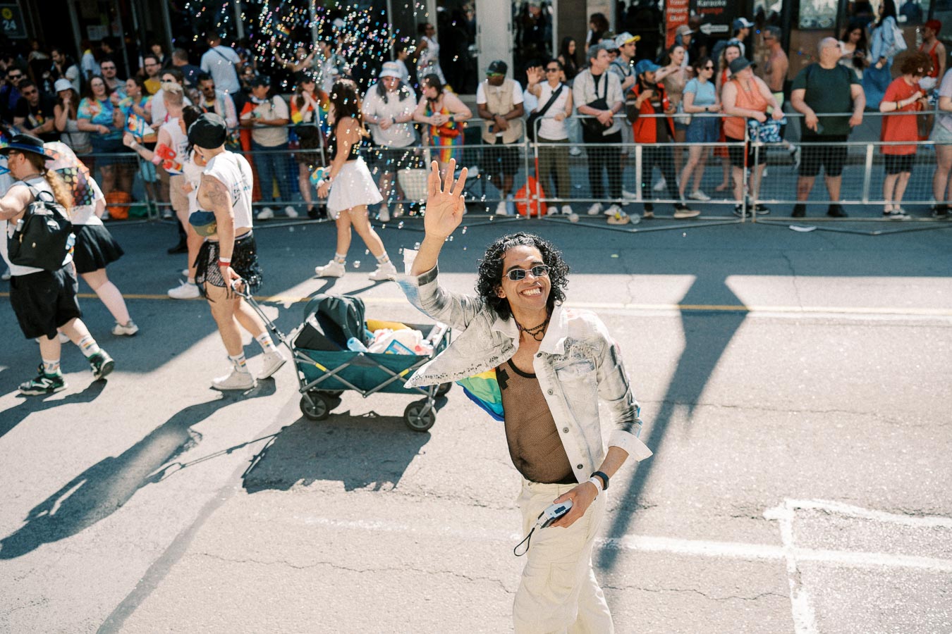 A lively scene from a parade featuring a person waving to the crowd, surrounded by bubbles and festive participants.