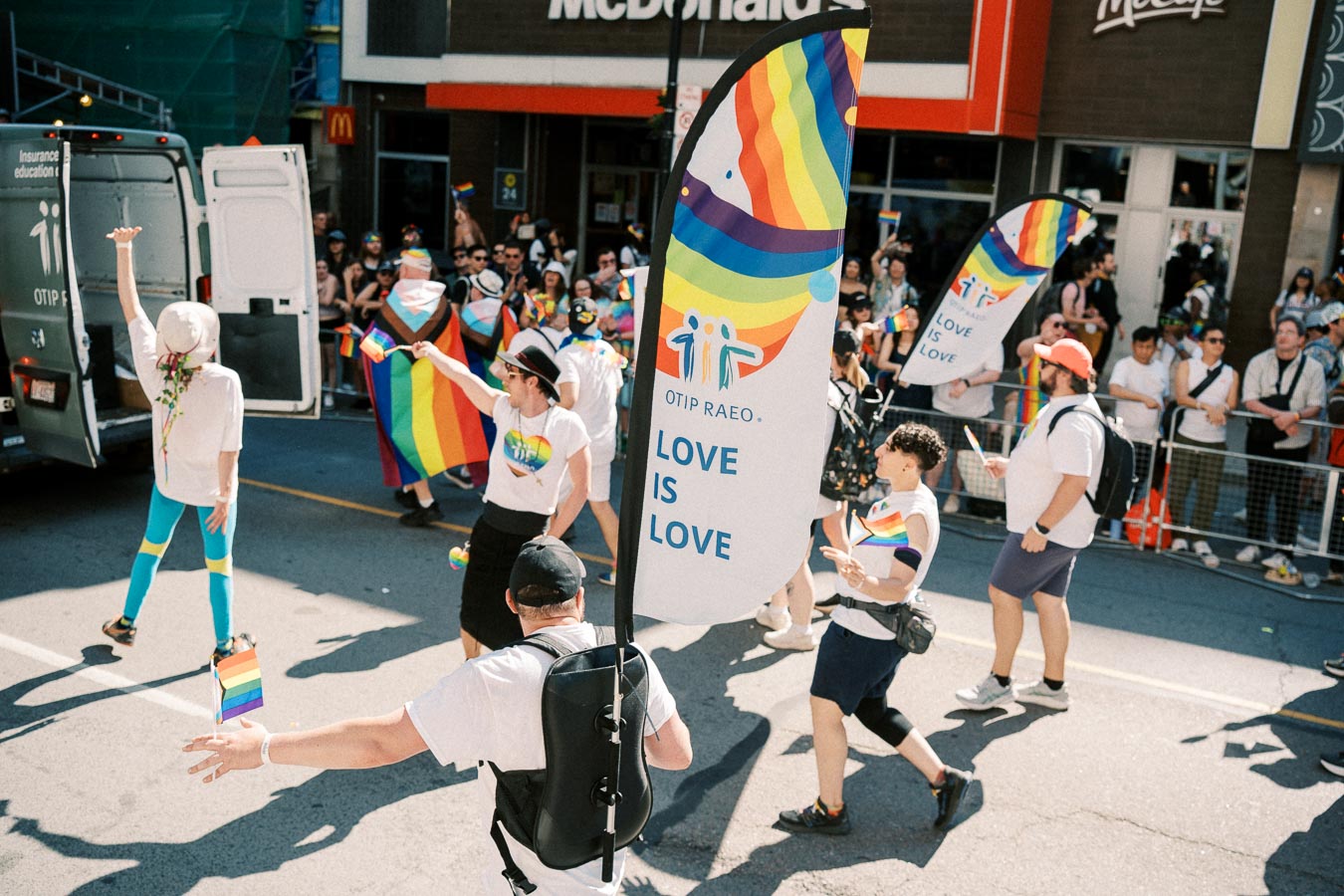 Participants in a pride parade celebrate with rainbow flags and banners reading 'Love is Love'.