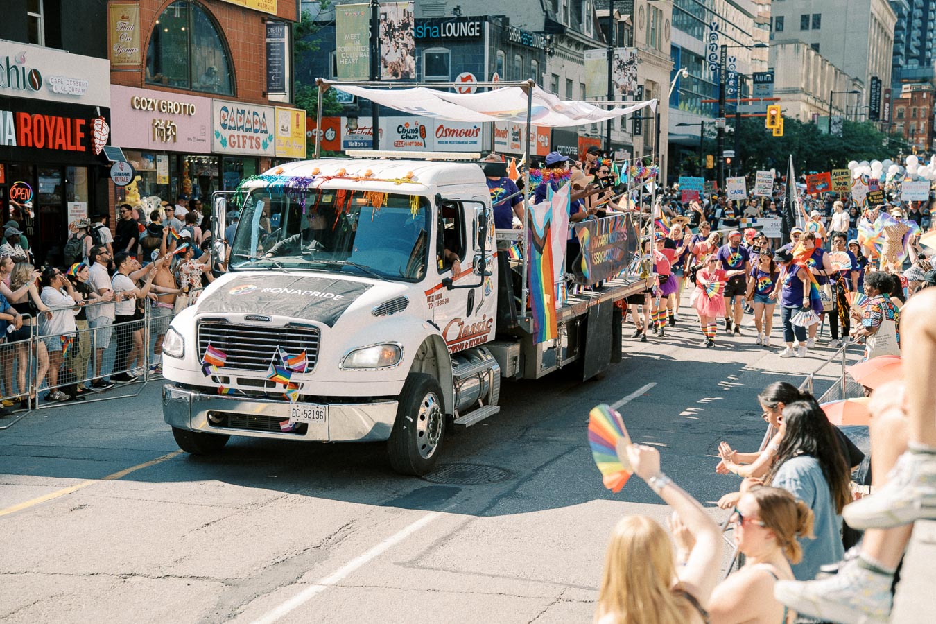 A vibrant pride parade featuring a decorated float and participants celebrating with rainbow flags and attire on a bustling city street.