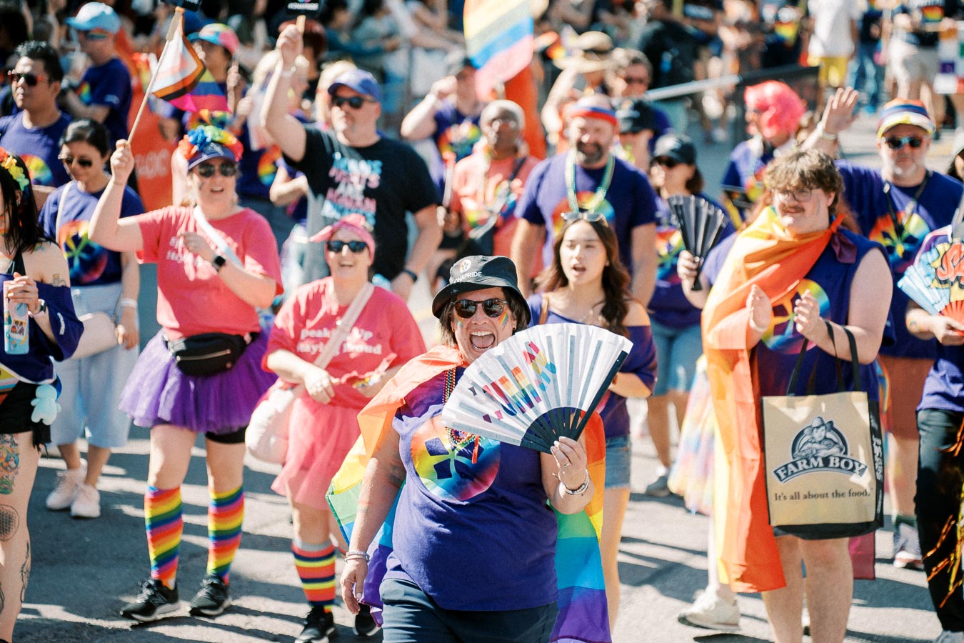 Participants at a pride parade joyfully march with rainbow flags and colorful attire, celebrating diversity and inclusion.