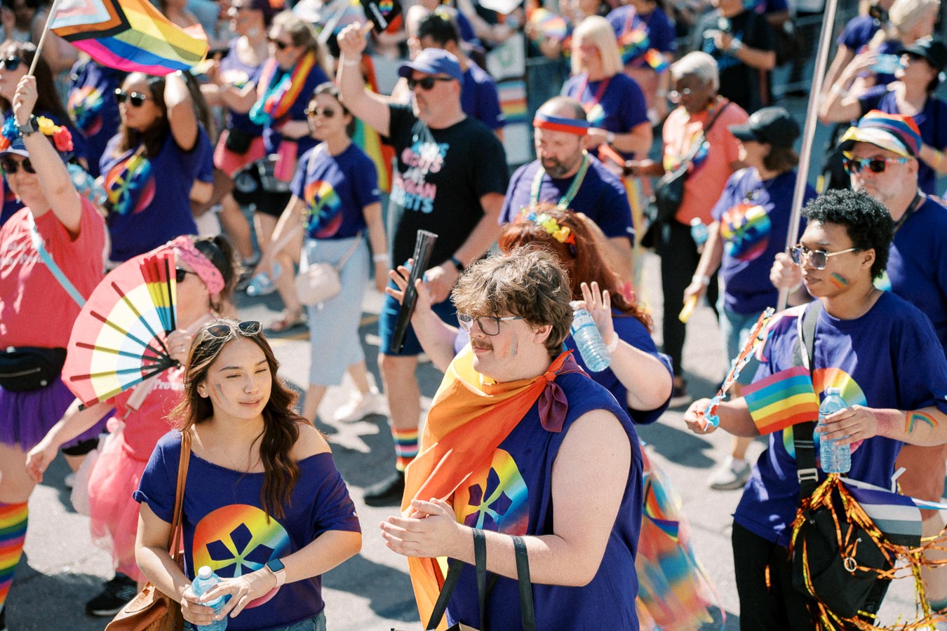 Participants in a pride parade wearing rainbow-themed clothing and accessories, celebrating diversity and inclusion.