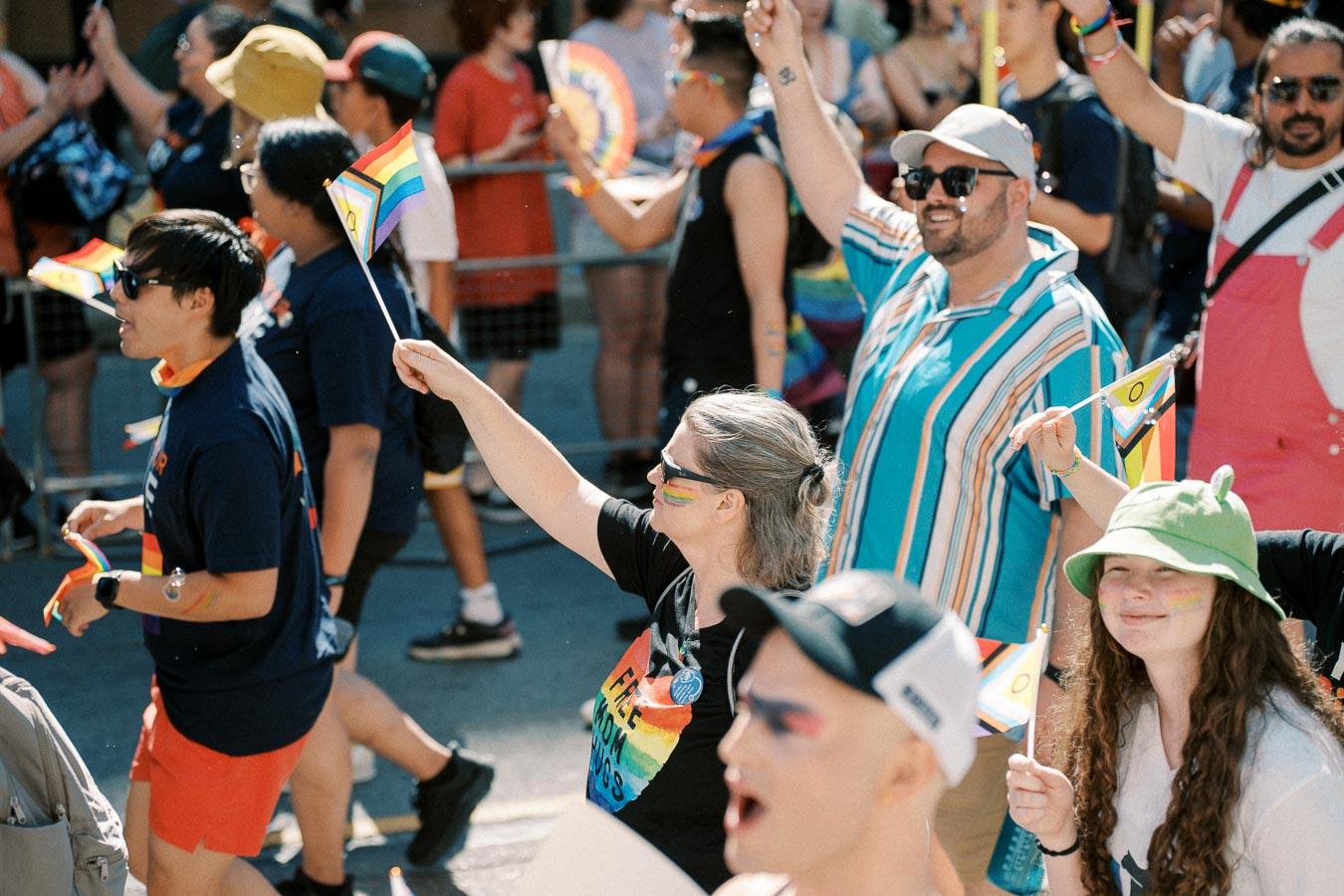 Participants in a pride parade celebrate with rainbow flags and colorful attire, showing support for the LGBTQ+ community.