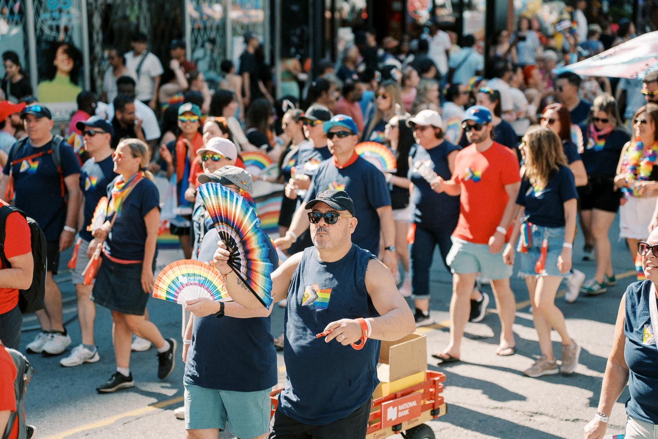 Participants in a pride parade celebrate with rainbow fans and vibrant clothing, showcasing support for the LGBTQ+ community.