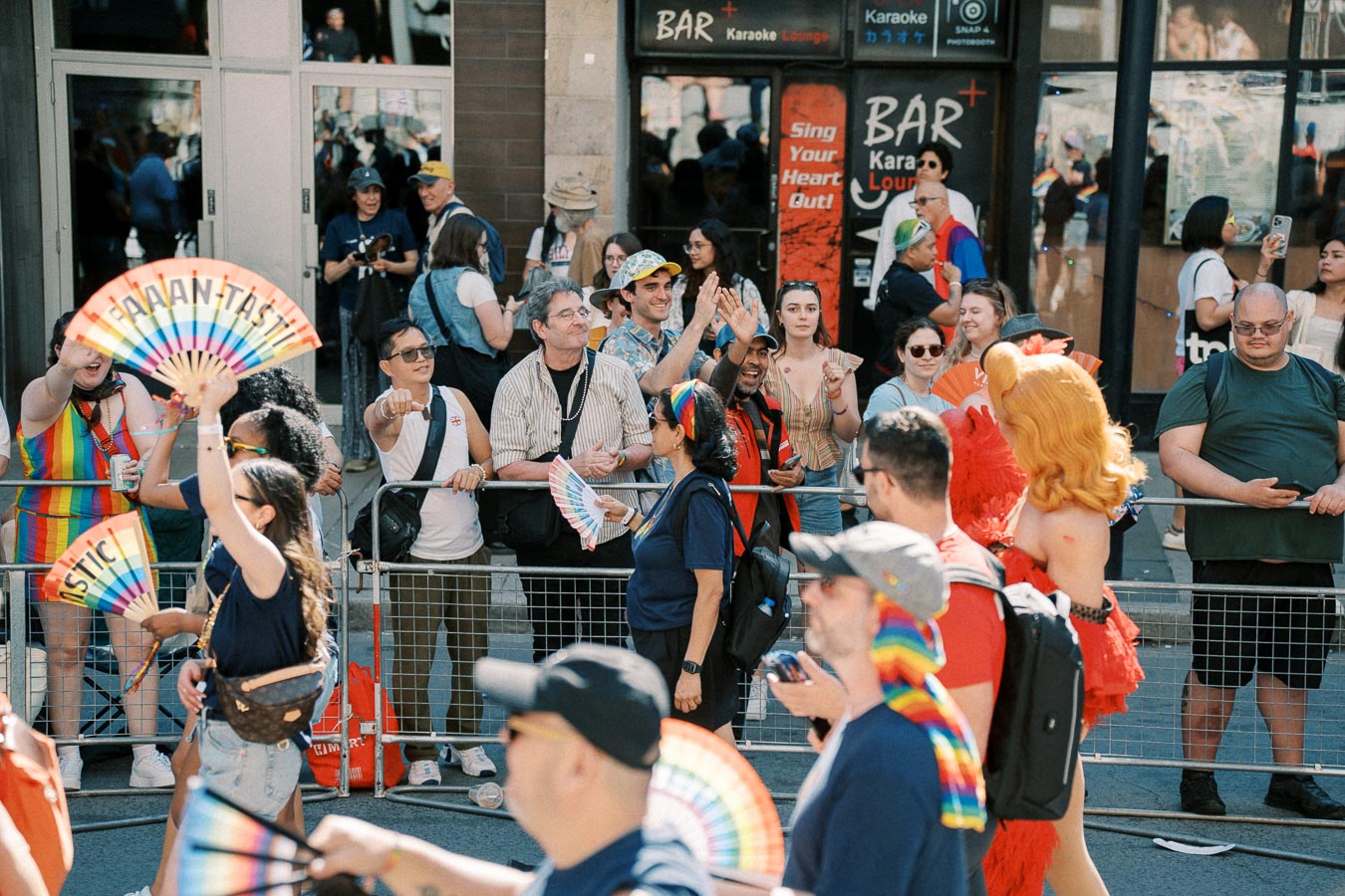 A vibrant pride parade scene with participants and spectators celebrating with rainbow fans and colorful attire.