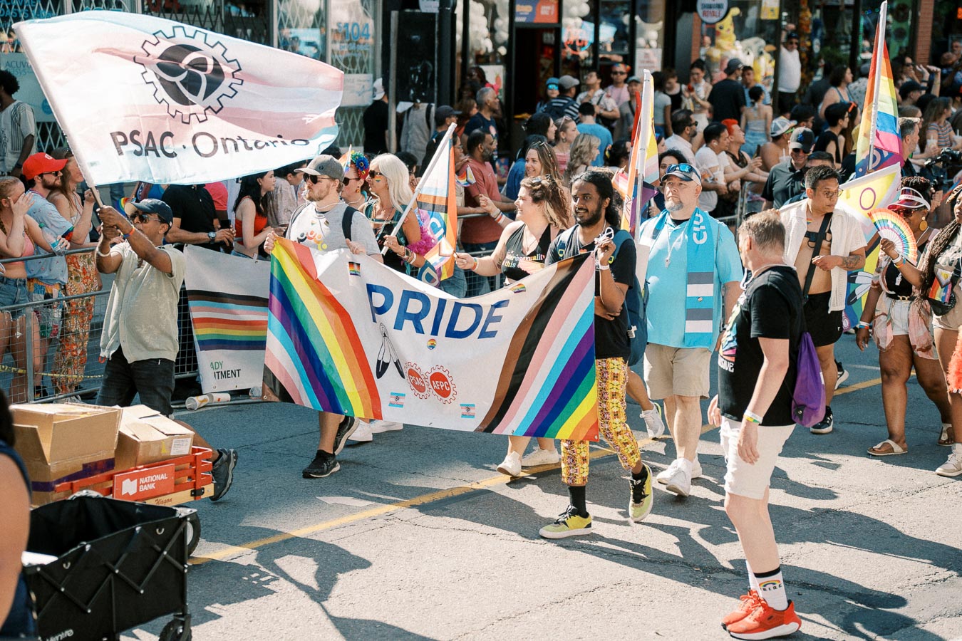 Participants march in a Pride parade, carrying a vibrant banner and flags, celebrating diversity and inclusion.
