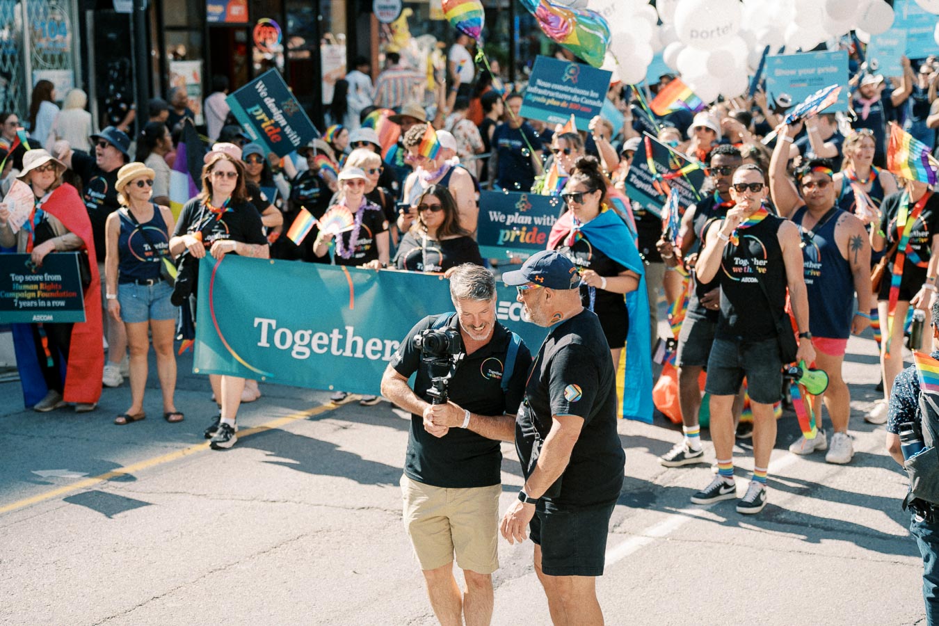 Participants in a pride parade march down the street, holding rainbow flags and banners with messages of inclusivity and pride.