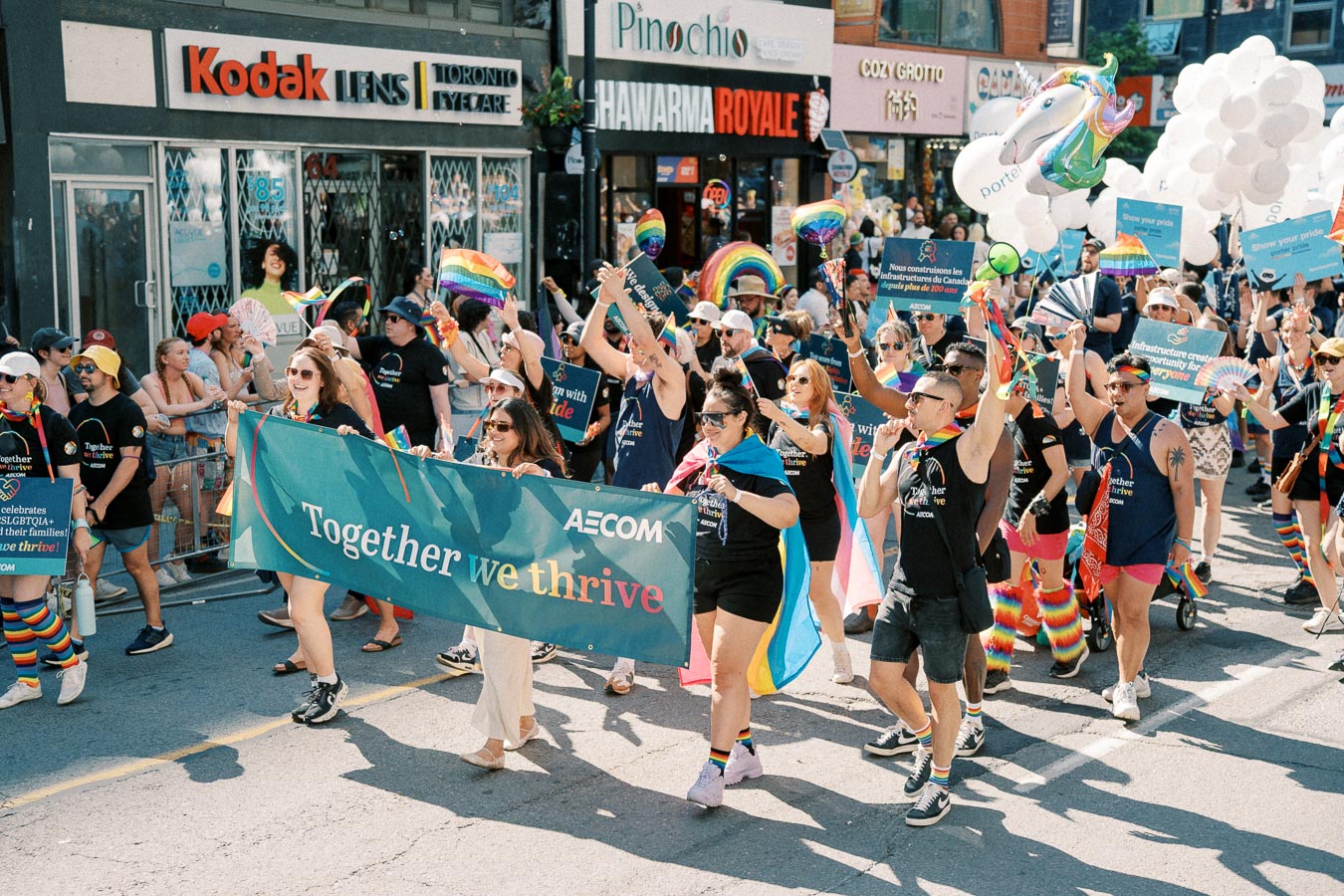 Participants in a pride parade march with a banner reading 'Together we thrive', celebrating diversity and inclusion.