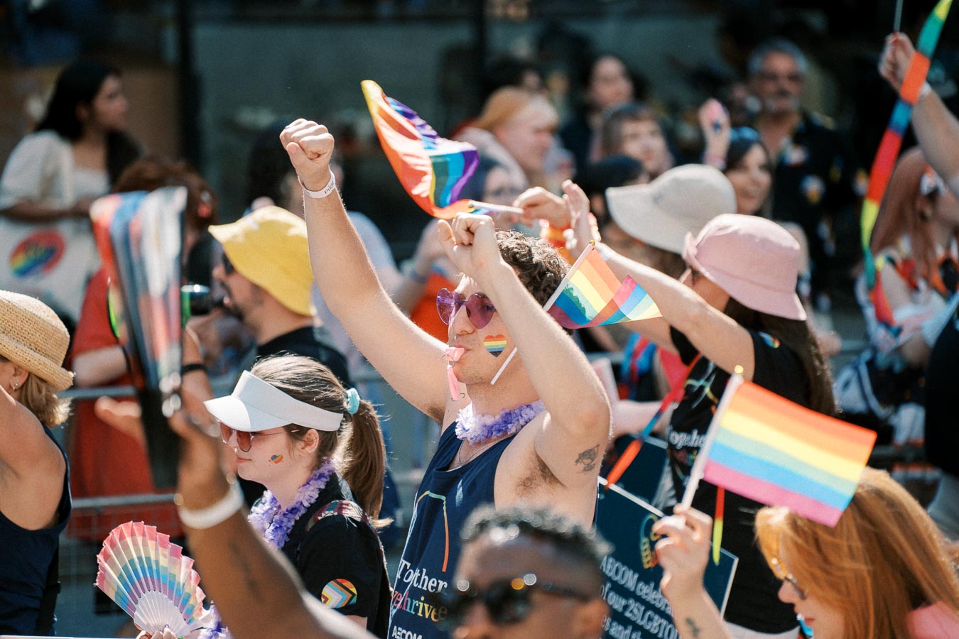 Participants at a pride parade joyfully wave rainbow flags and wear colorful accessories, celebrating diversity and inclusion.