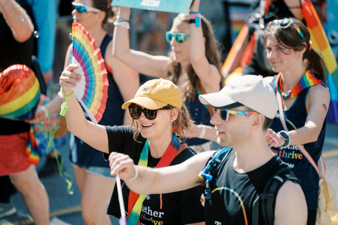 Participants at a pride parade joyfully wave rainbow-colored fans and wear colorful accessories, celebrating diversity and inclusion.