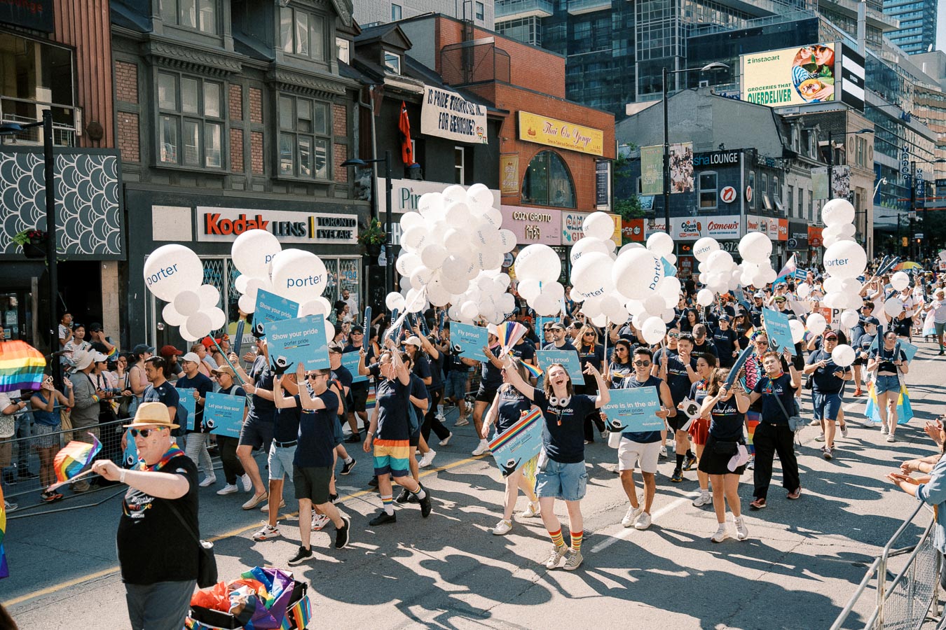 Participants in a vibrant parade march down a city street, holding white balloons and signs, celebrating with rainbow flags and accessories.