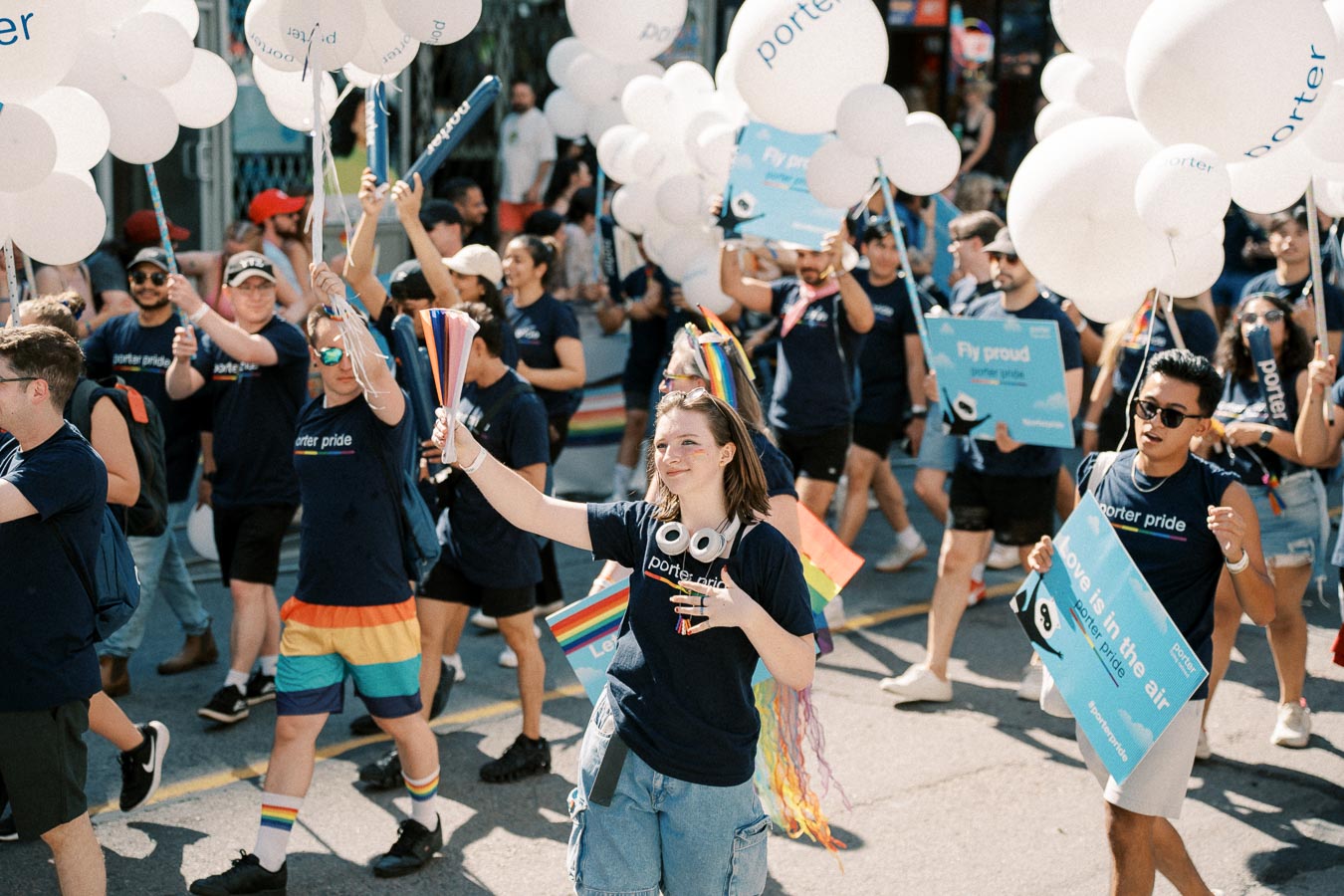 Participants in a pride parade celebrate with balloons and signs promoting inclusivity and pride, wearing 'porter pride' shirts.