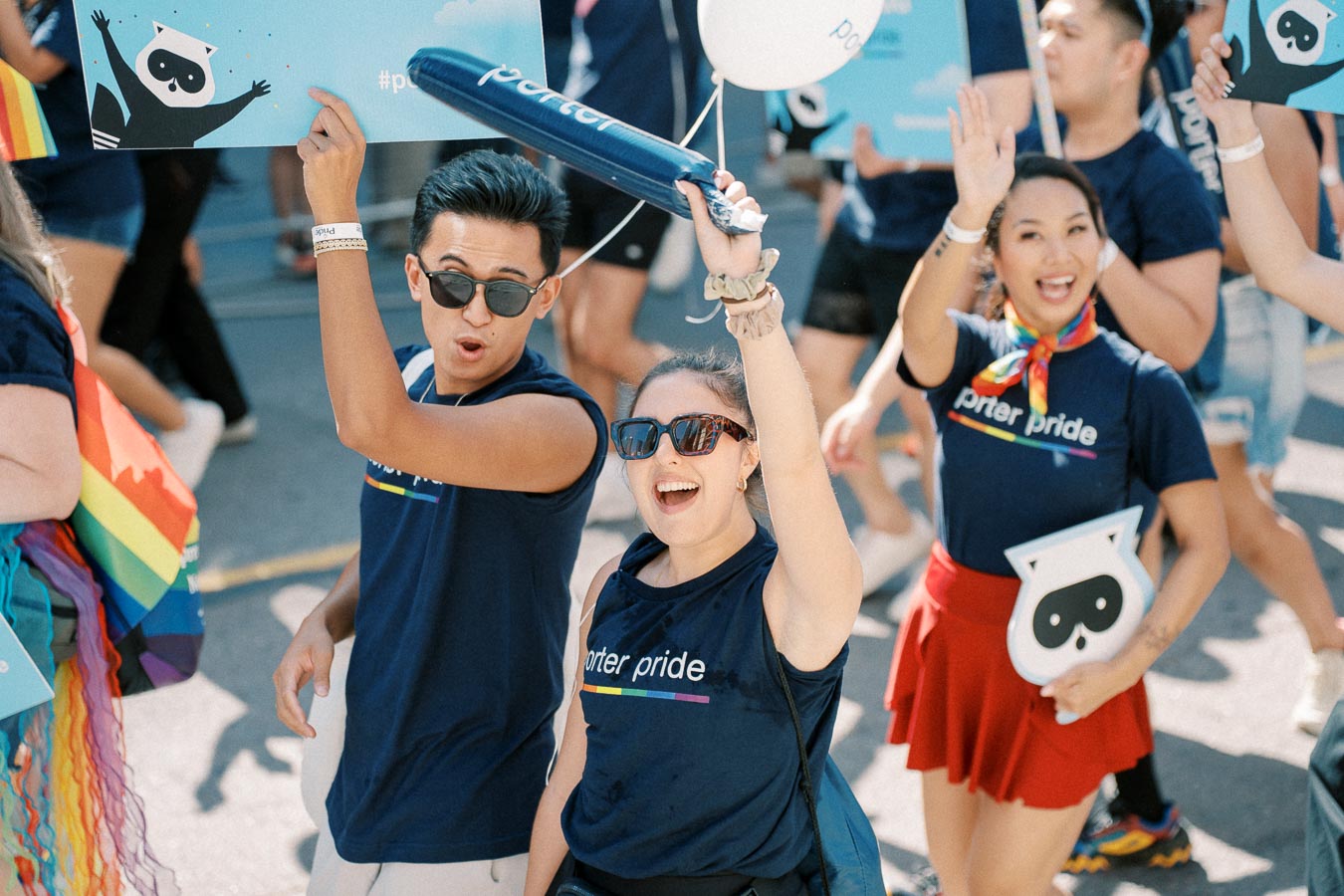 Participants in a pride parade celebrate with enthusiasm, wearing 'porter pride' shirts and holding signs and balloons.