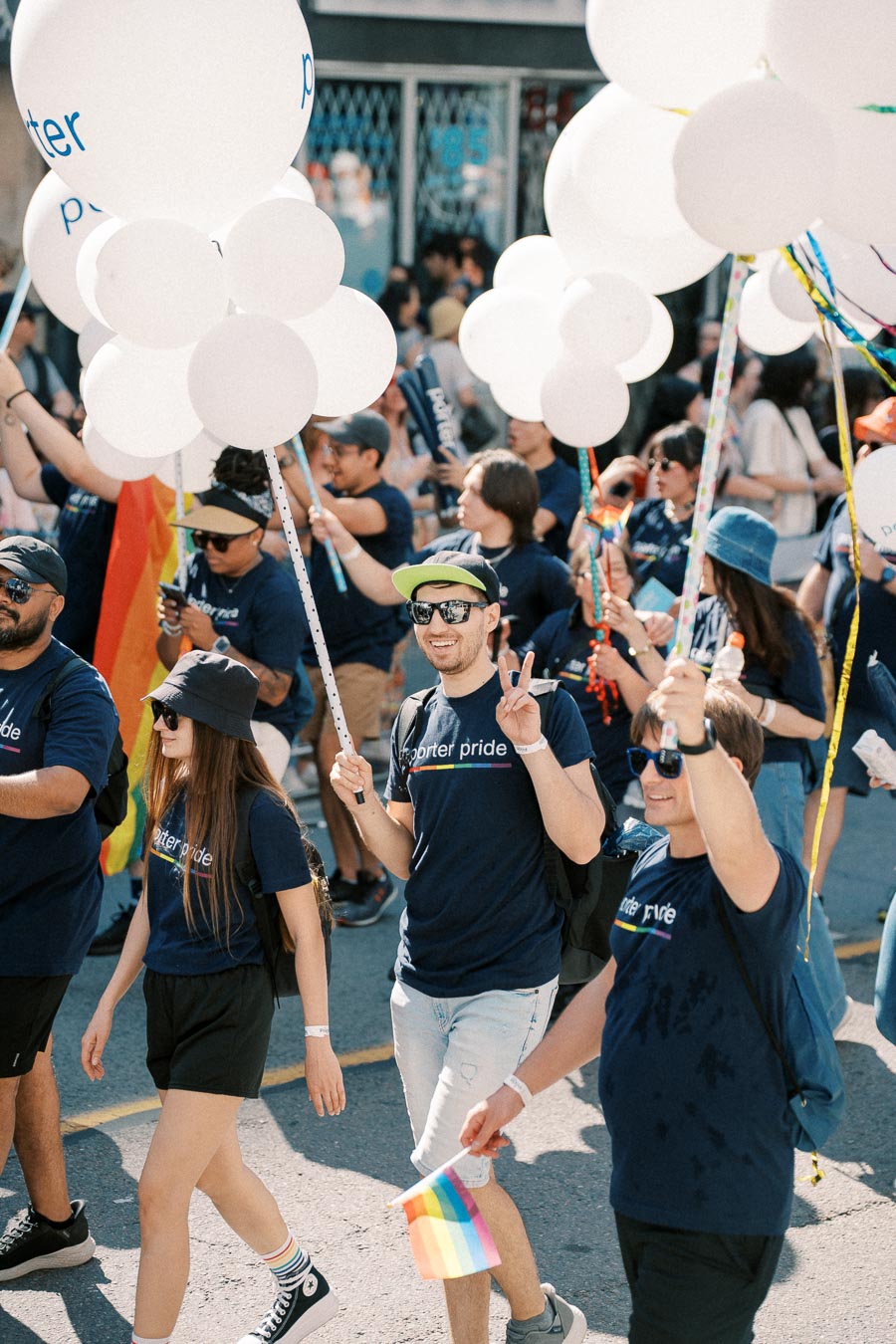 Participants in a pride parade march joyfully, holding white balloons and rainbow flags, wearing matching shirts that read 'porter pride'.