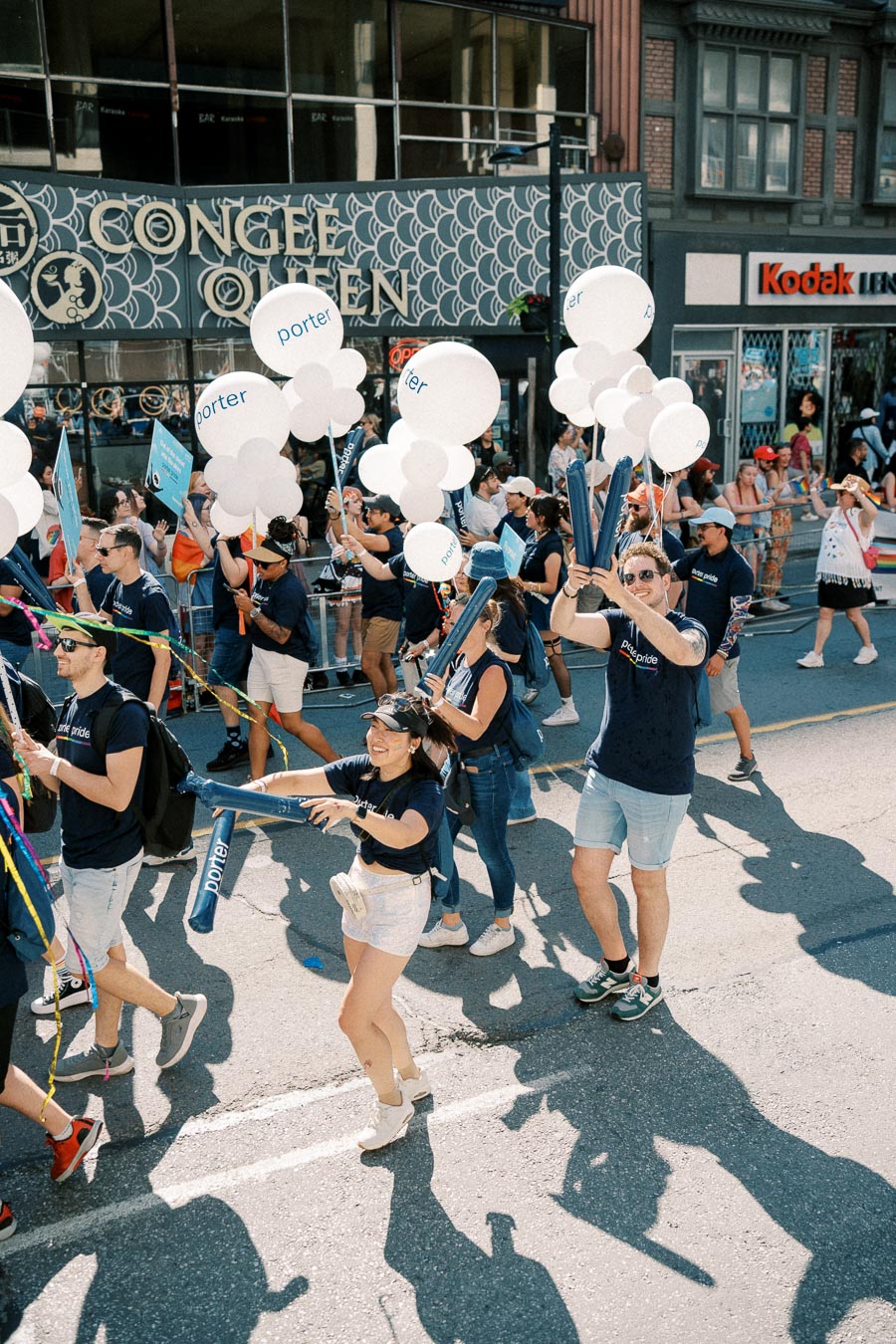 Participants in a parade hold 'porter' balloons, marching past a building with 'Congee Queen' signage.