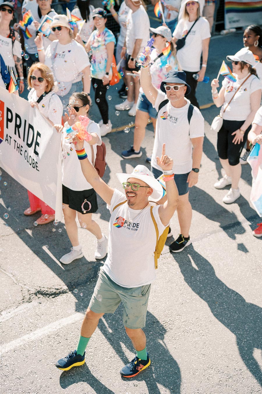 Participants in a Pride parade celebrate with rainbow flags and bubbles, wearing themed shirts and accessories.