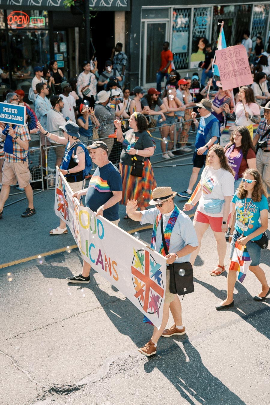 Participants in a pride parade march with a banner reading 'Proud Anglicans', celebrating diversity and inclusion.