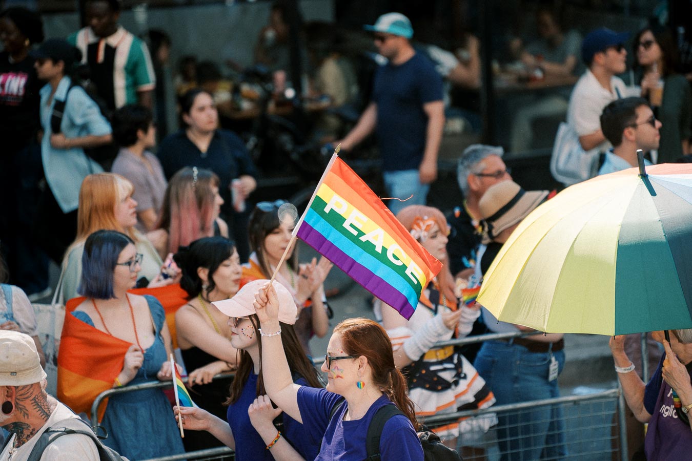 A vibrant scene at a pride event, featuring a rainbow flag with 'PEACE' and a rainbow umbrella, symbolizing unity and diversity.