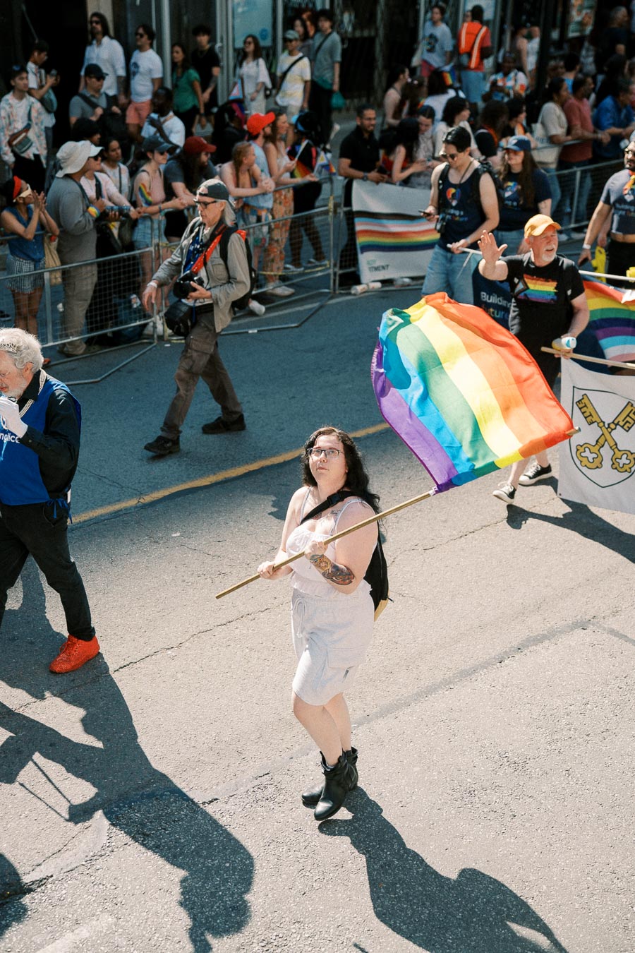 A participant in a pride parade holds a rainbow flag, symbolizing LGBTQ+ pride, while walking down a street lined with spectators.