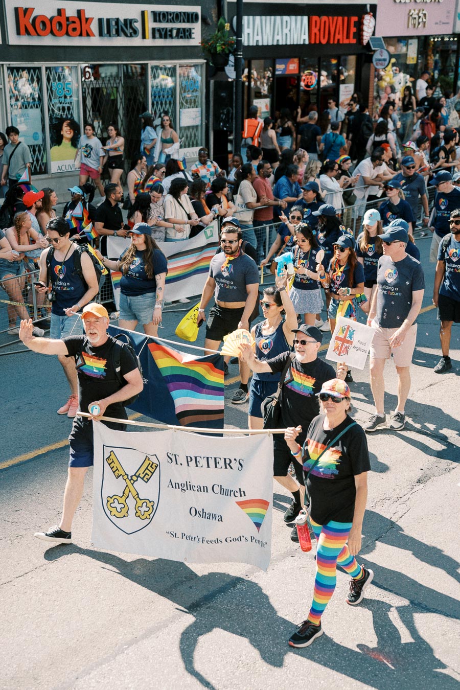 Participants from St. Peter's Anglican Church, Oshawa, march in a pride parade, showcasing support with rainbow-themed attire and banners.