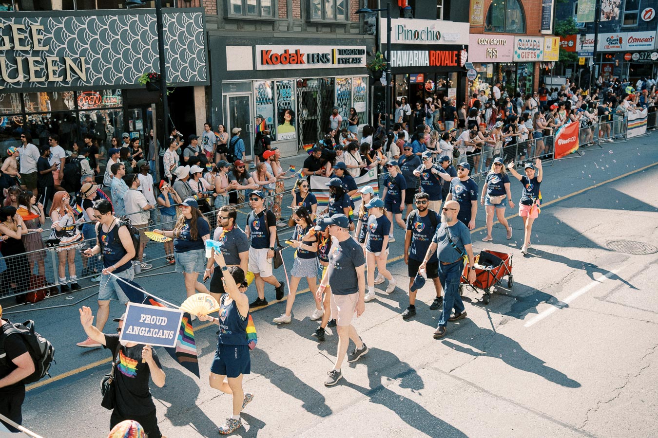 Participants in a pride parade march with a 'Proud Anglicans' sign, showcasing support and inclusivity.