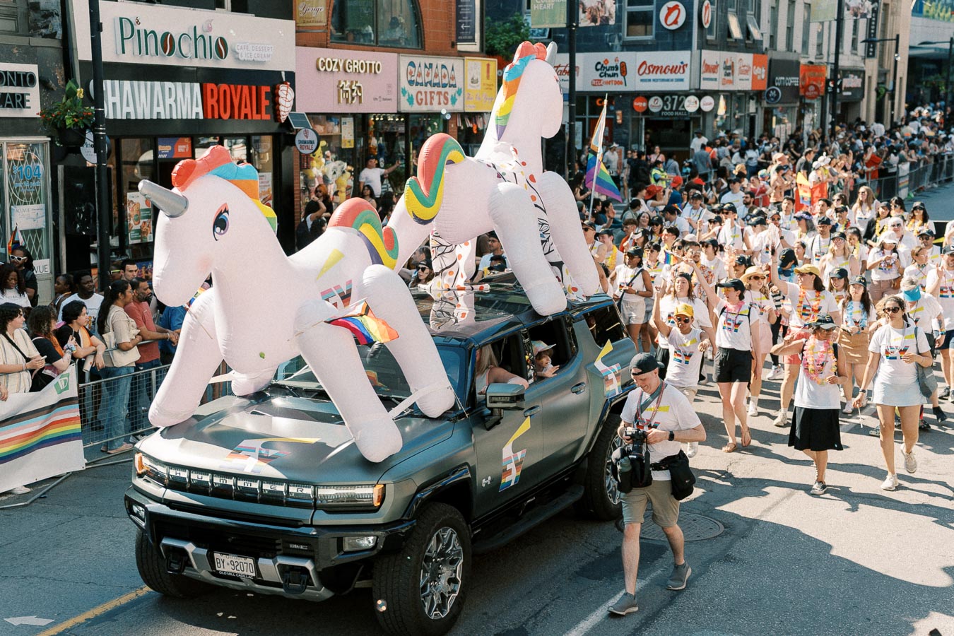 A vibrant parade features a large inflatable unicorn atop a vehicle, with participants wearing rainbow-themed attire, celebrating diversity and inclusion.