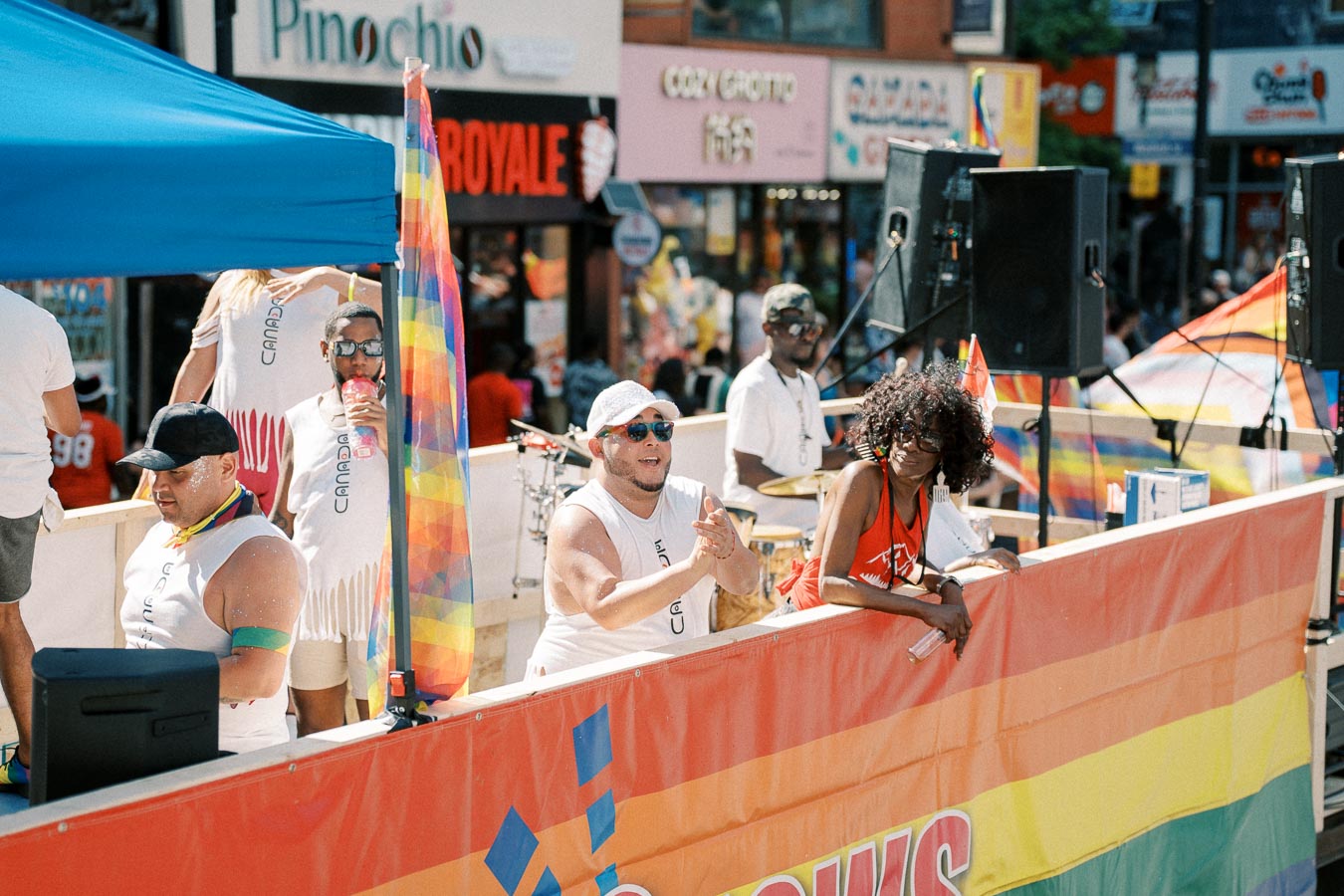 Participants on a parade float celebrate at a pride event, surrounded by rainbow flags and banners.