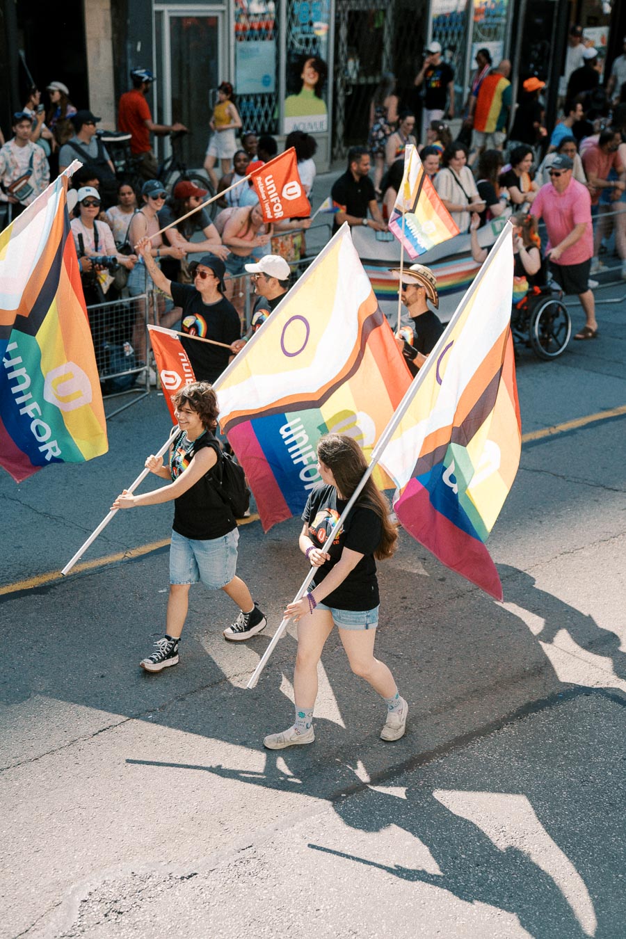 Participants in a parade march with rainbow flags featuring the Unifor logo, celebrating diversity and inclusion.