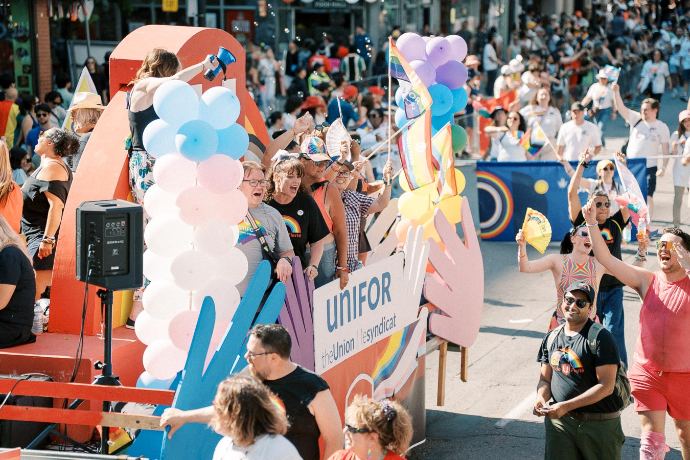 Participants celebrate on a colorful parade float with rainbow flags and balloons, representing Unifor the Union.