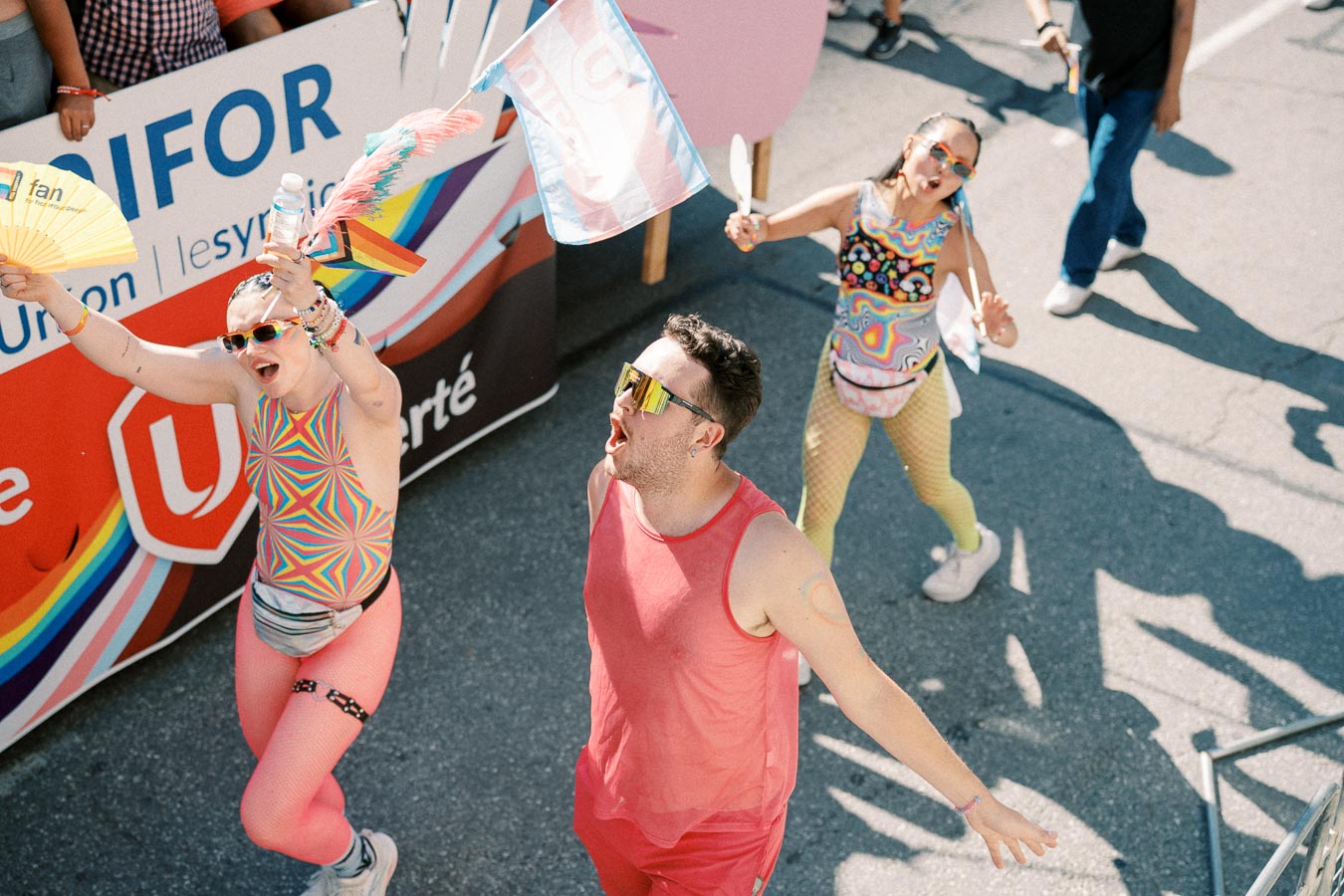 Participants in vibrant attire celebrate at a pride parade, waving flags and fans.