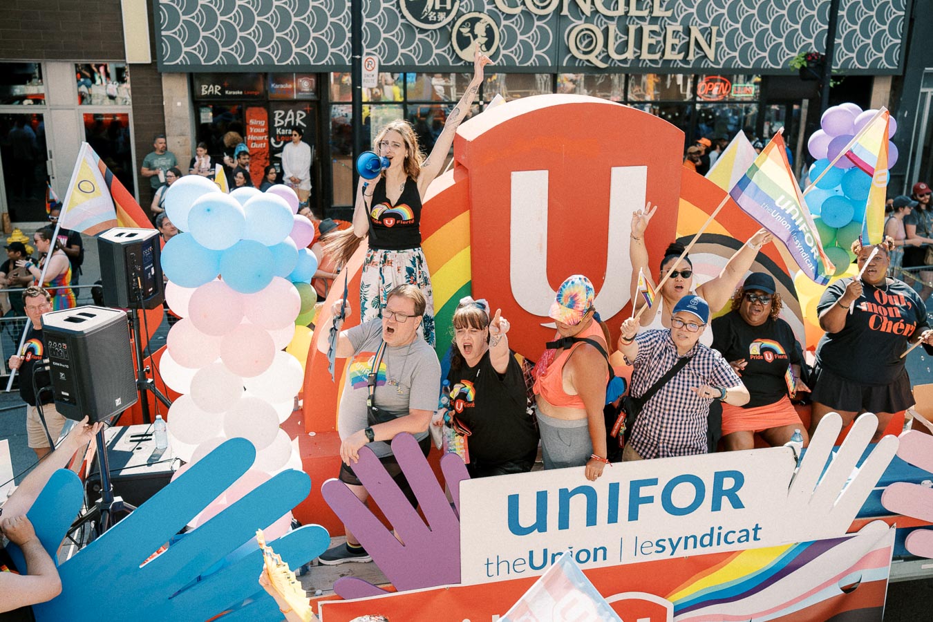 A vibrant pride parade float featuring Unifor members celebrating with rainbow flags and balloons.