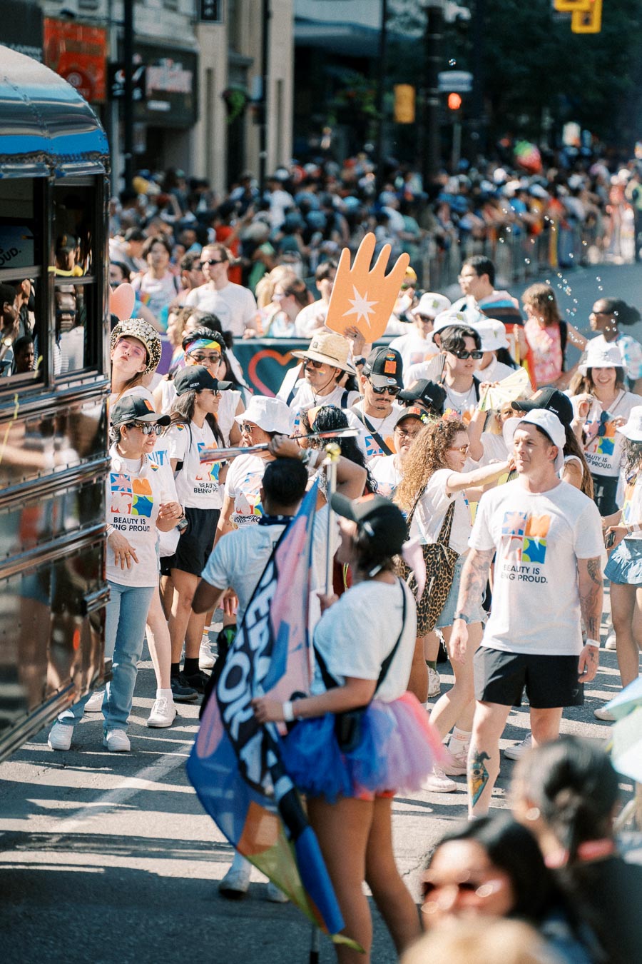 Participants in a pride parade wearing themed T-shirts and carrying flags and signs, celebrating diversity and inclusion.