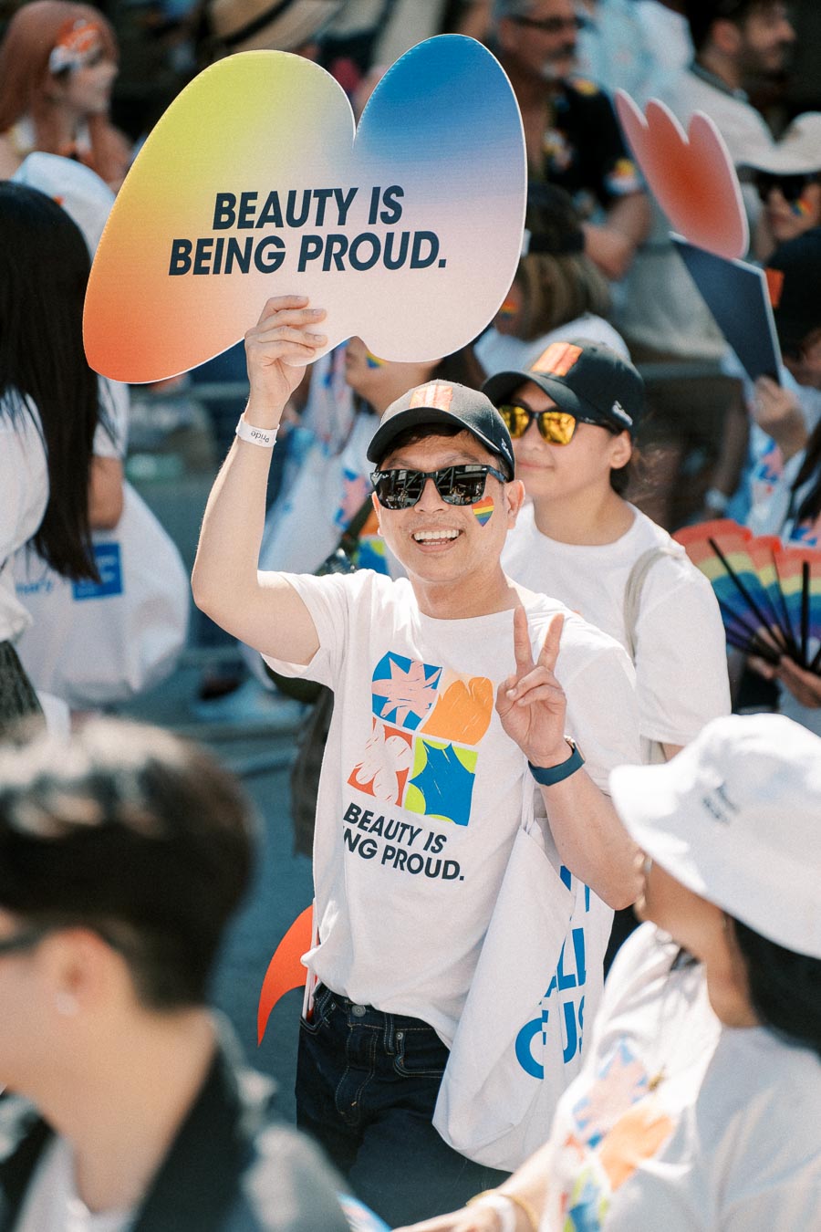 A participant at a pride parade holds a sign reading 'Beauty is Being Proud,' celebrating diversity and inclusion.