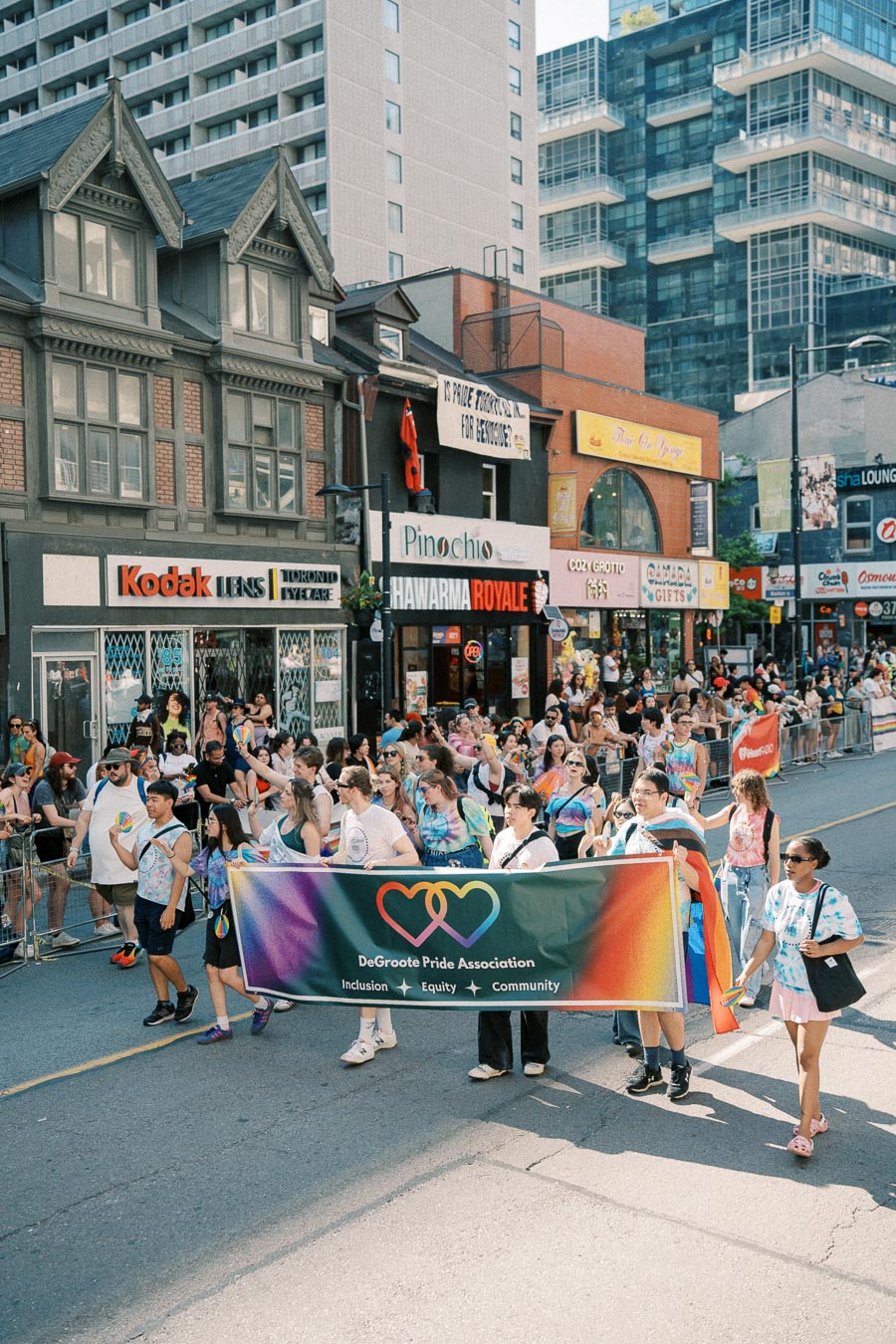 Participants in a pride parade march with a banner for the DeGroote Pride Association, promoting inclusion, equity, and community.