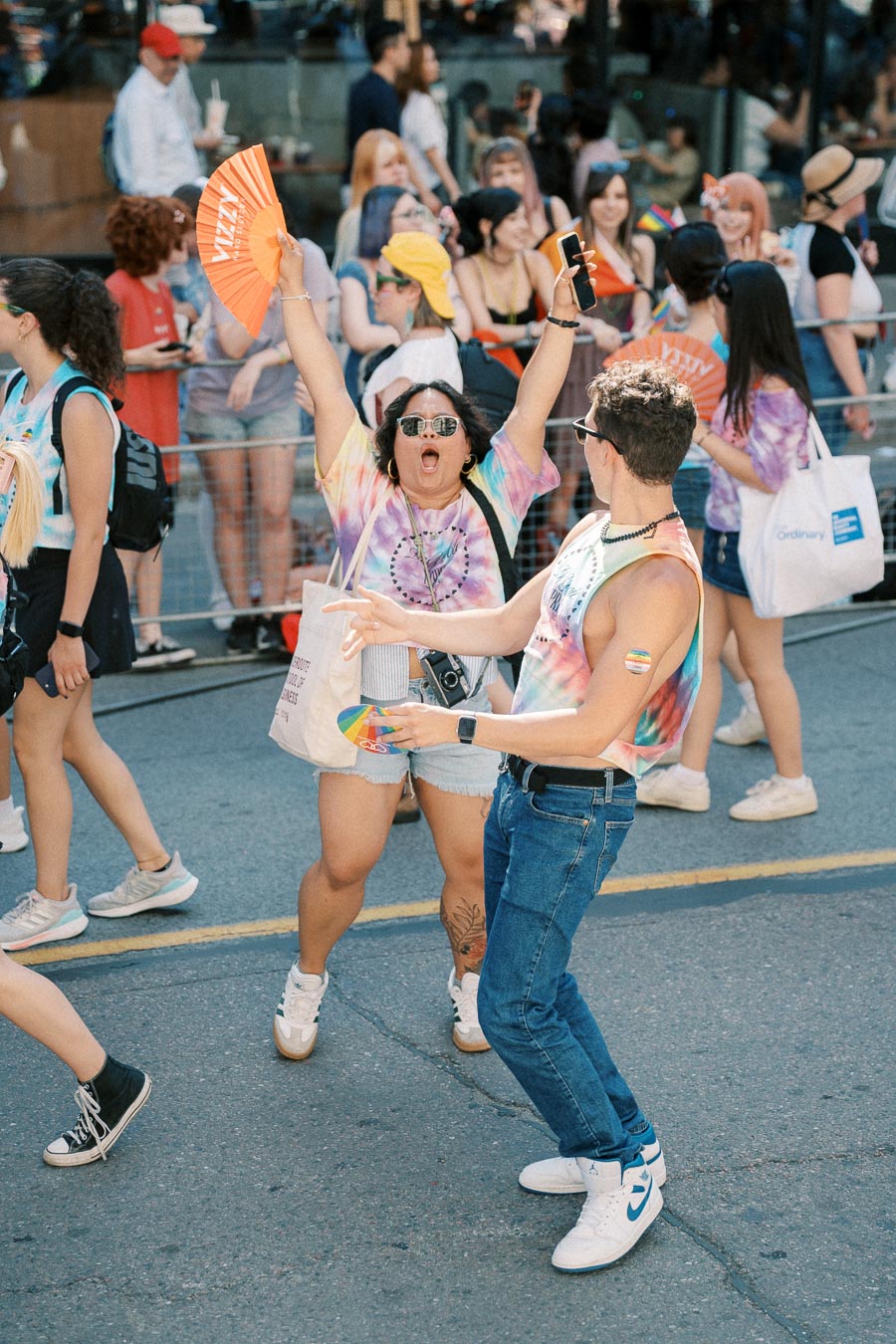 Participants joyfully celebrate at a pride parade, wearing vibrant tie-dye shirts and holding colorful fans.